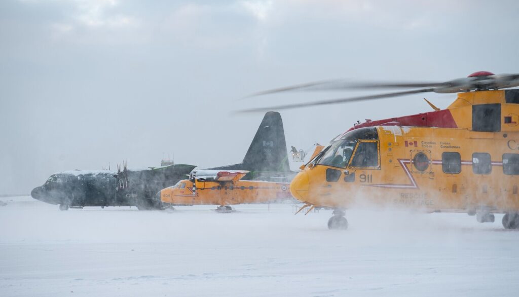 Canadian Forces CH-149 Cormorant search and rescue helicopter and CC-130 Hercules aircraft on a snow-covered airfield
